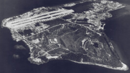 Aerial view of a small island that is densely build upon with buildings and an airport runway
